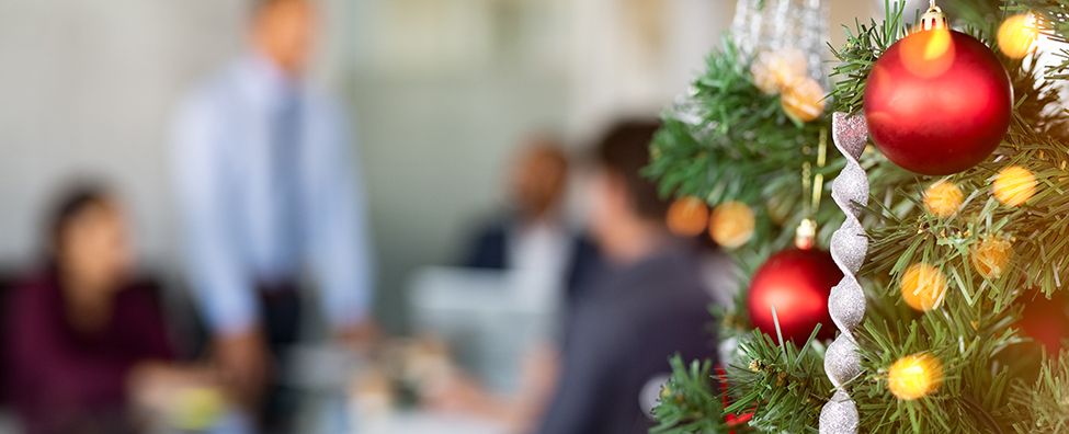 Close up of decorated Christmas tree in office with business people working in background.