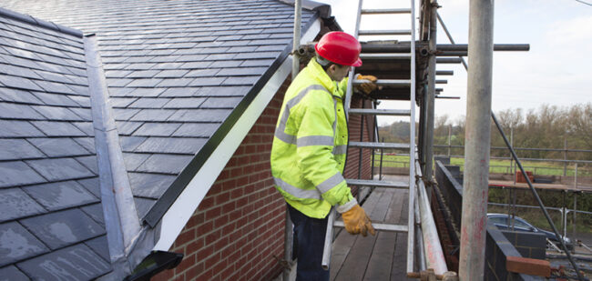 Young builder using a ladder on the roof of a building site