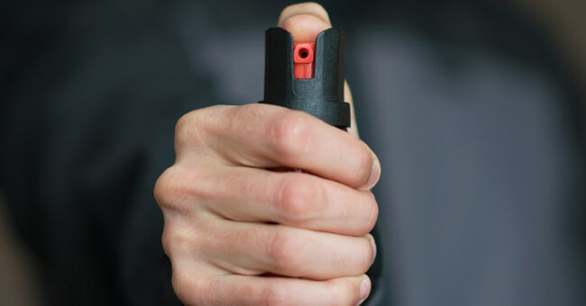 Man holding pepper spray in his hand. Self-defense. Blur background, close up.
