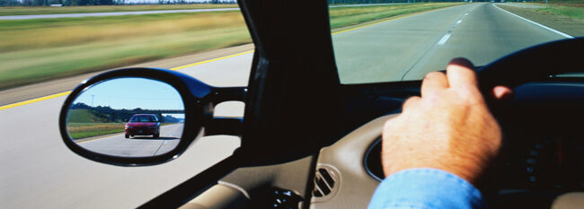 Close up of hand on steering wheel, view out windshield and view in side rear view mirror