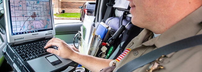 Deputy works on laptop in parked squad car