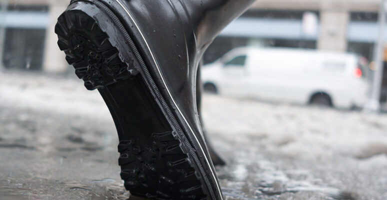 Close-up of a woman's boots walking through slush ice and snow on a wintery day in the city.