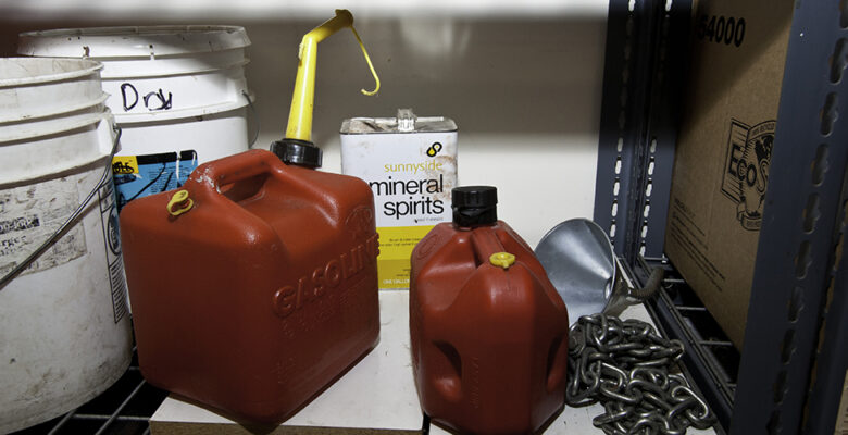 Two portable fuel containers sit on storage shelf with can of mineral spirits and buckets