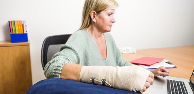 A female office worker at her desk with an elevated wrist to relieve the pain and swelling of a sprain.