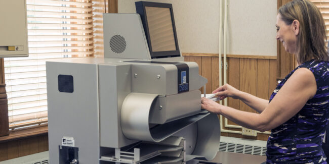 Woman demonstrates using electronic voting equipment: high-speed scanner.