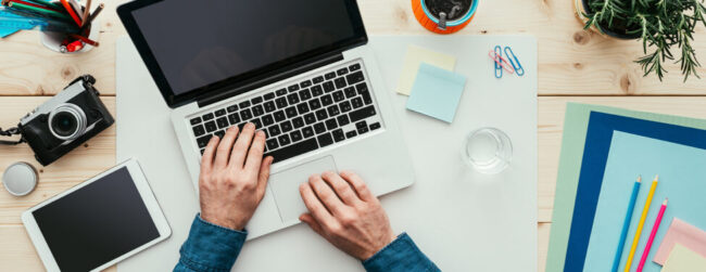 Working at desk in his office, he is typing with a laptop, top view with camera and tablet computer on desk