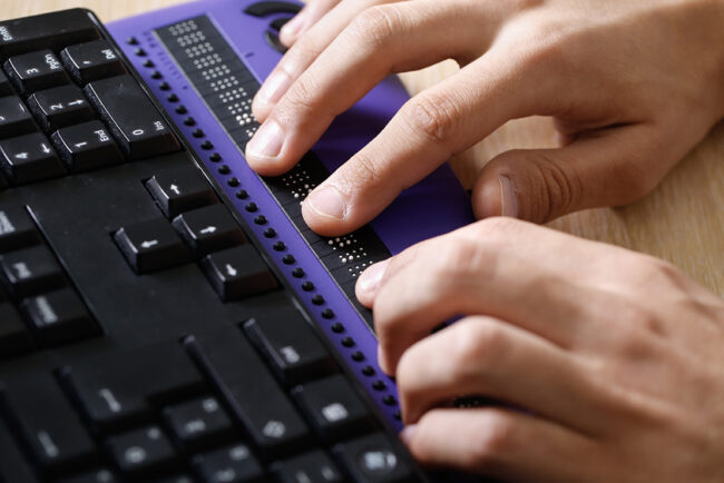 Blind person using computer with braille computer display and a computer keyboard.