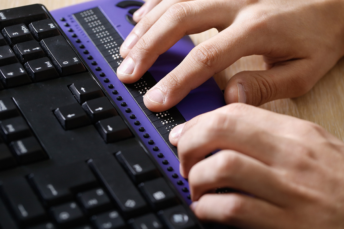 Blind person using computer with braille computer display and a computer keyboard.