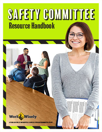 Cover of Safety Committee Resource Handbook. Woman on cover standing in front of table holding a clipboard. Coworkers talk in the background.