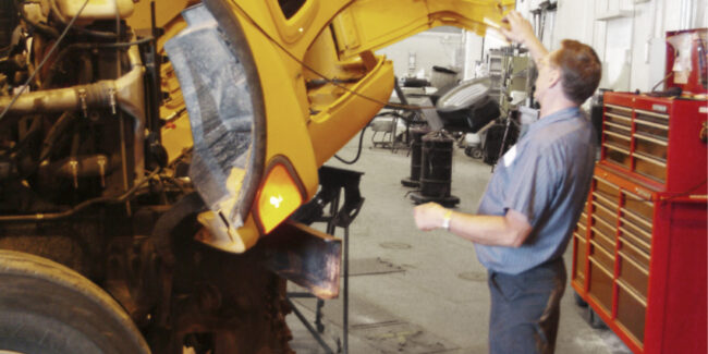 Public works shop where man works on large truck shows walkway is clear of clutter all the way to the back of the shop.