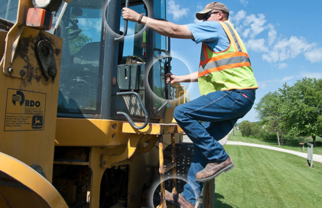 Man climbs into large construction vehicle while holding on with two hands and one foot is on step rail.