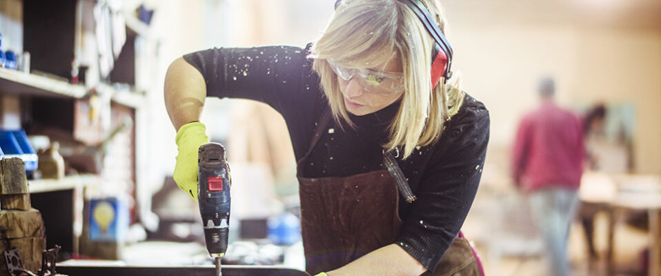 Woman uses power drill wearing eye, ear and hand protective equipment