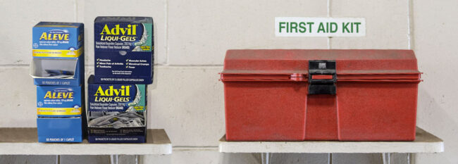 Boxes of Advil Liqui-gels and Aleve on shelf next to red first aid kit.