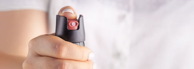 Woman holding pepper spray. Hand view only. Blurred white shirt in the background.