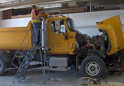Lac qui Parle County Highway Department worker on a rolling work platform fixing a dump truck.