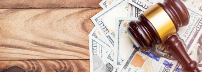 Gavel placed atop of a pile of $100 bills. Wood table background.