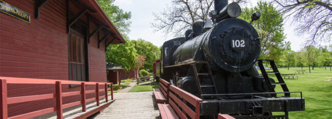 Property Coverage for Historical Societies Black steam engine in historical Murray County town. Pulling up next to red wooden station with benches.