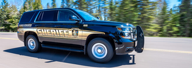 Lake County Sheriff SUV driving fast down a road. Blurred trees in the background.