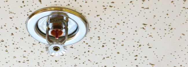 Close-up of sprinkler on drop ceiling tile in office,