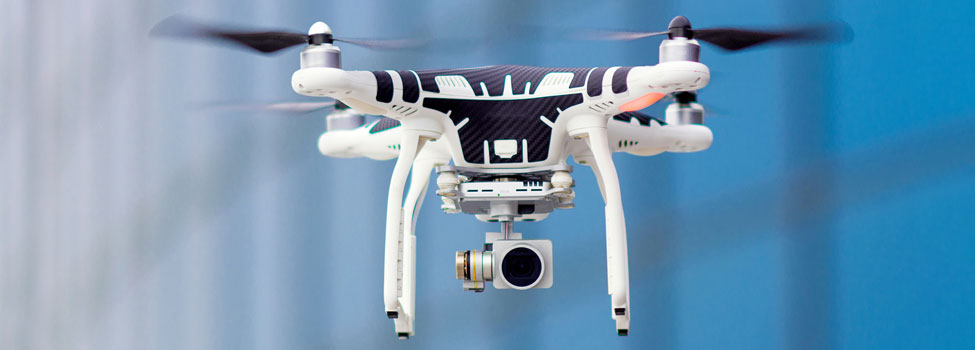 White drone flying through air with blurred out office building in the background. Drone carrying camera.