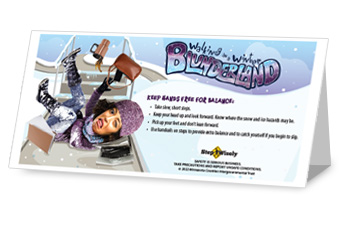 Step Wisely Walking in a Winter Blunderland table tent. "Keep hands free for balance." Woman with large cartoonish head has fallen down the stairs and landed on back with legs and arms in air. Computer, coffee cup, folders and purse are falling through the air.