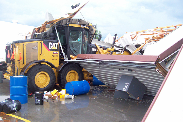 Large equipment truck with storm damaged building collapsed around it along with other debris