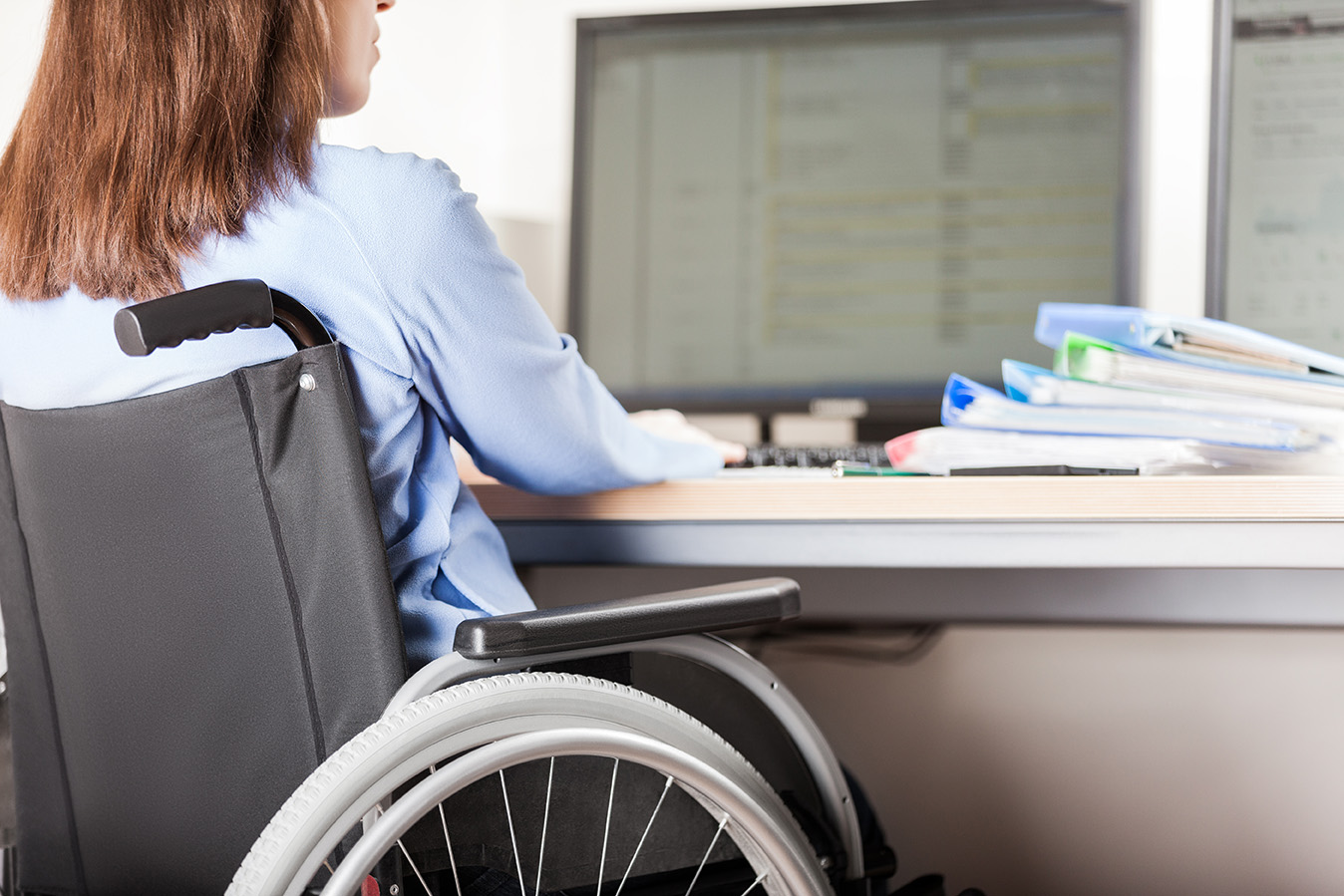 Young business woman person sitting in a wheelchair working office desk computer