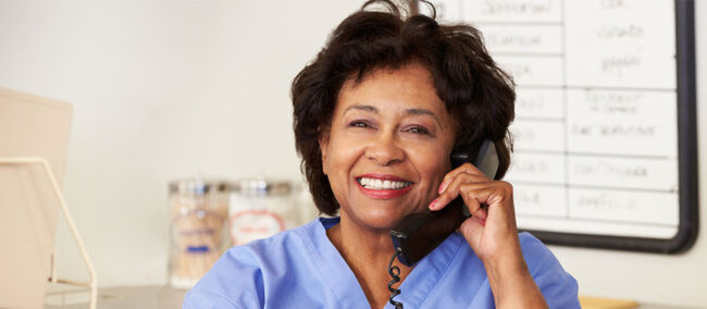 Smiling African American nurse talks on phone in an office setting.