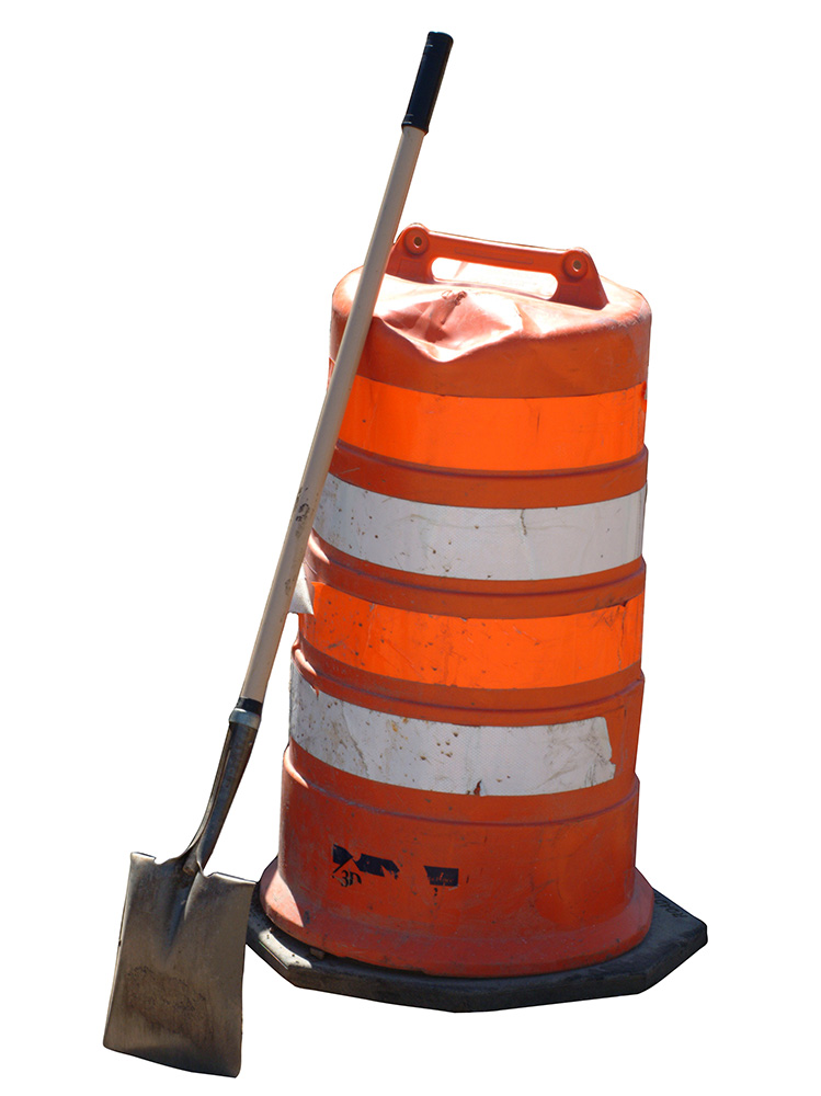 Construction zone hazard barrel with shovel leaning against it against a white background