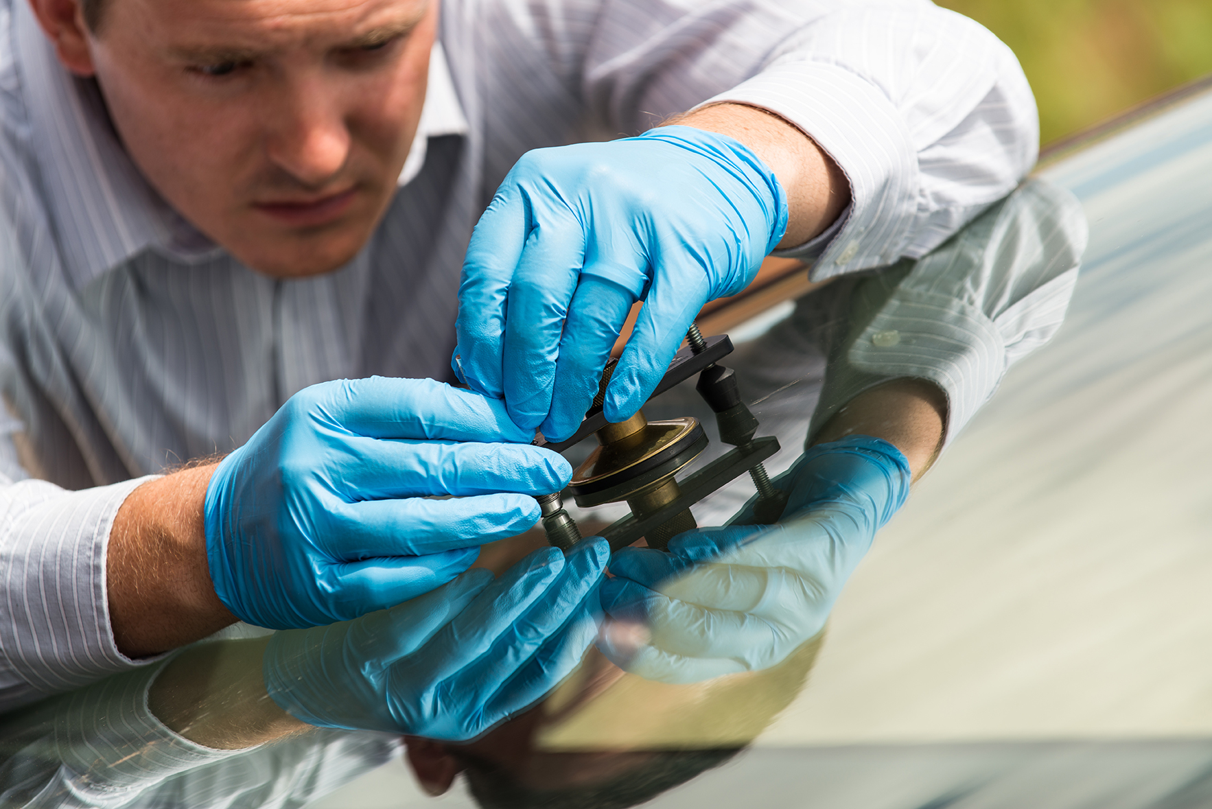 Man repairing chip in an automobile windshield.