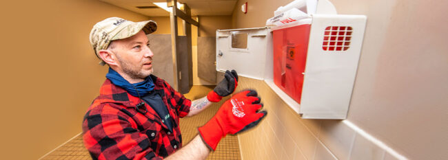 Janitor emptying sharps needle container in a bathroom.