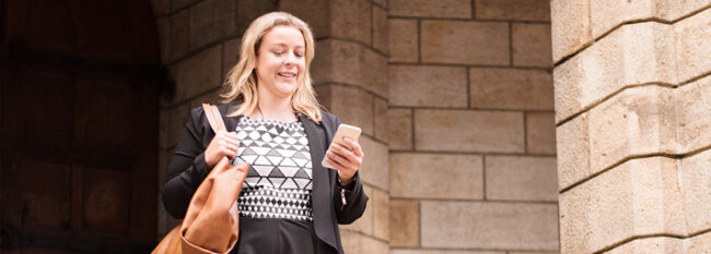 Woman leaving work and looking at cell phone.