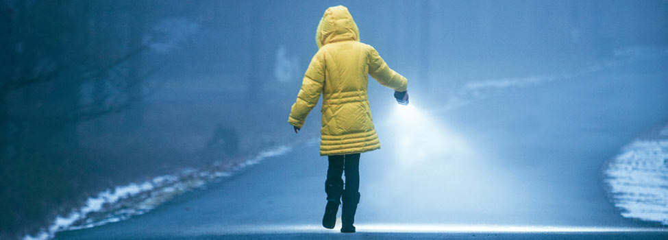 Girl in yellow jacket walking in the fog with a flashlight.