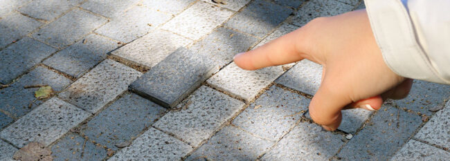 Woman pointing finger at raised brick on pathway.