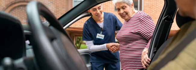 Volunteer helps elderly woman into car.