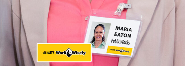 Woman wearing employee badge "Maria Eaton, Public Works" Has "Always Work Wisely" sticker on the bottom.