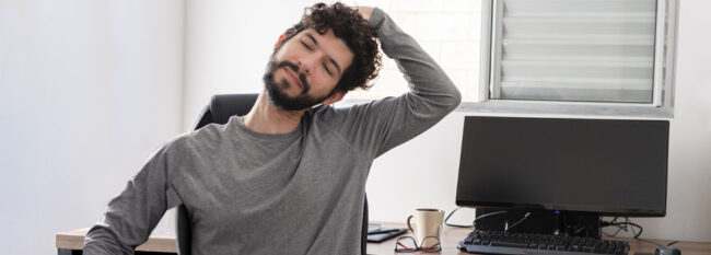 Man stretching neck at office desk.