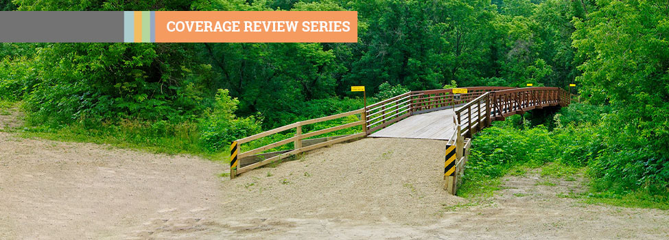Coverage Review Series - bike/walking bridge in woods with dirt path.