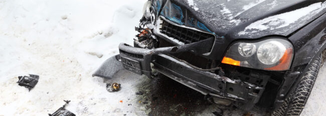 Black truck with front damage and pieces scattered in snow.