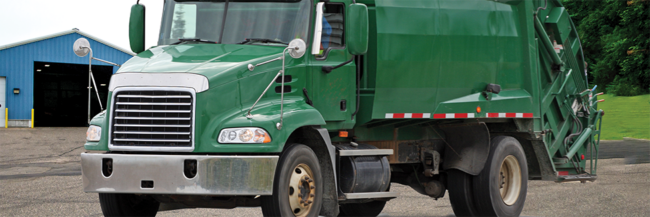 Green garbage truck is parked in front of a solid waste transfer station building