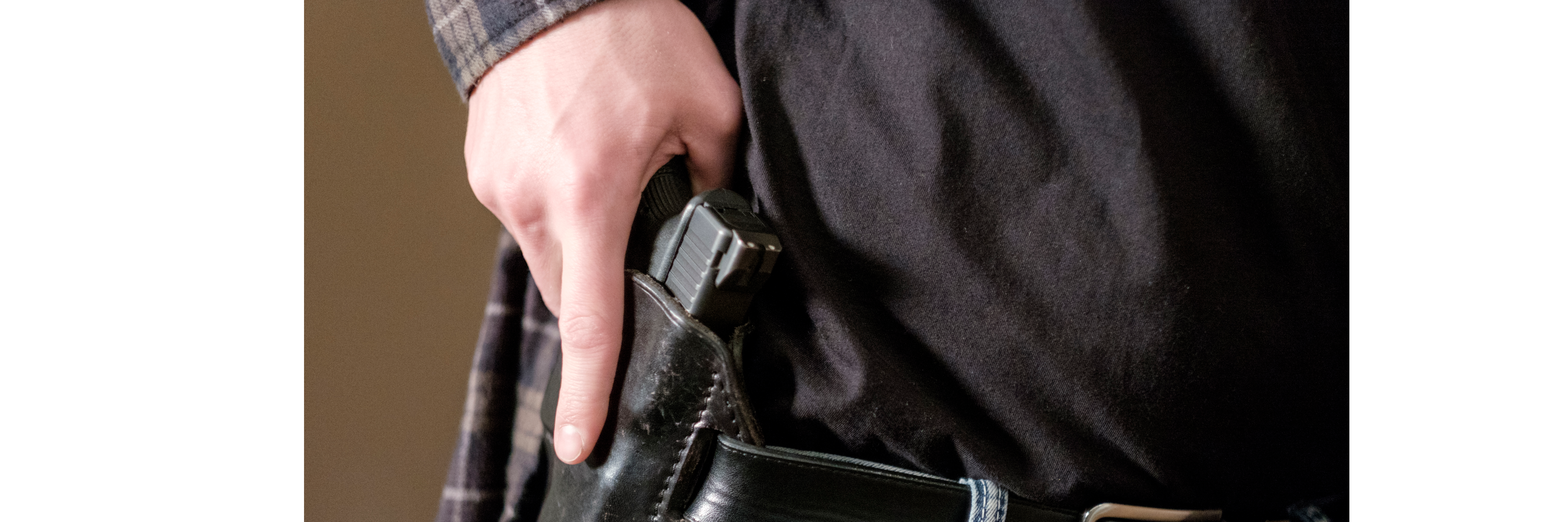 General male citizen holsters handgun at waist under shirt
