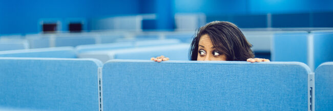 Woman peeks over cubicle wall in office space