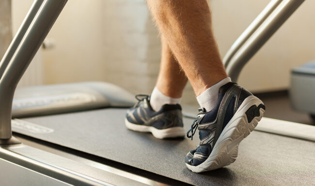 Close-up of man walking by treadmill