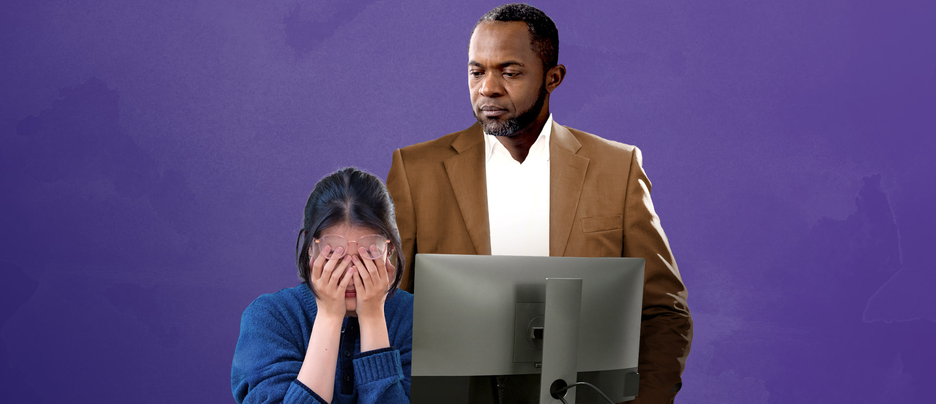 Concerned male supervisor looks at distraught female employee at desk. Female employee has hands over face.