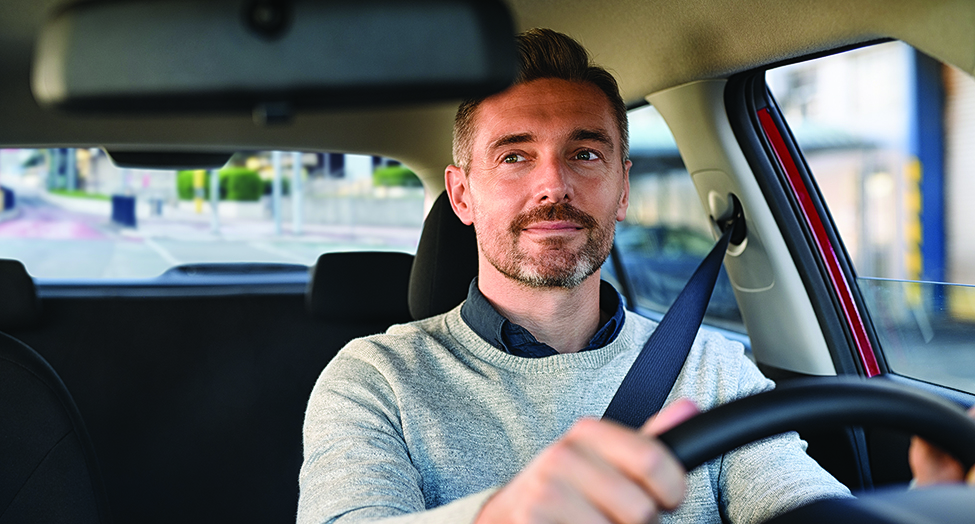 Mid adult casual man smiling while driving car and looking at mirror for reverse. Happy man feeling comfortable sitting on driver seat in his new car. Smiling mature businessman with seat belt on driving vehicle for transport and copy space.