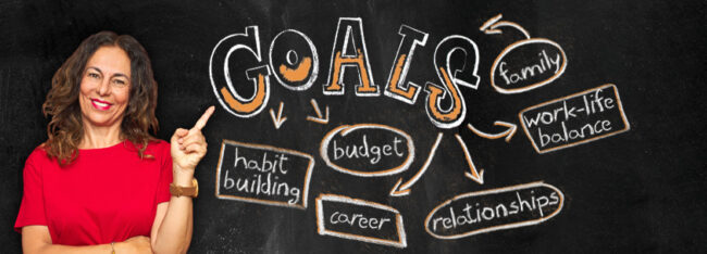 Woman stands next to chalk board pointing to word web with 