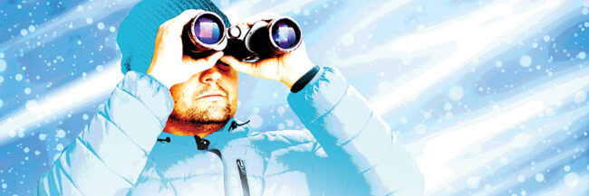 Man in blue stocking hat and winter jacket holds binoculars to eyes while snowstorm swirls around him