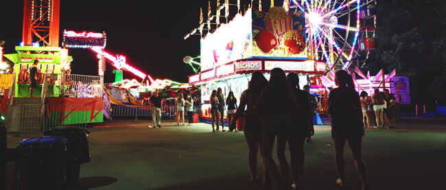 Night view of county fair: Ferris wheel, concession stand, attendees